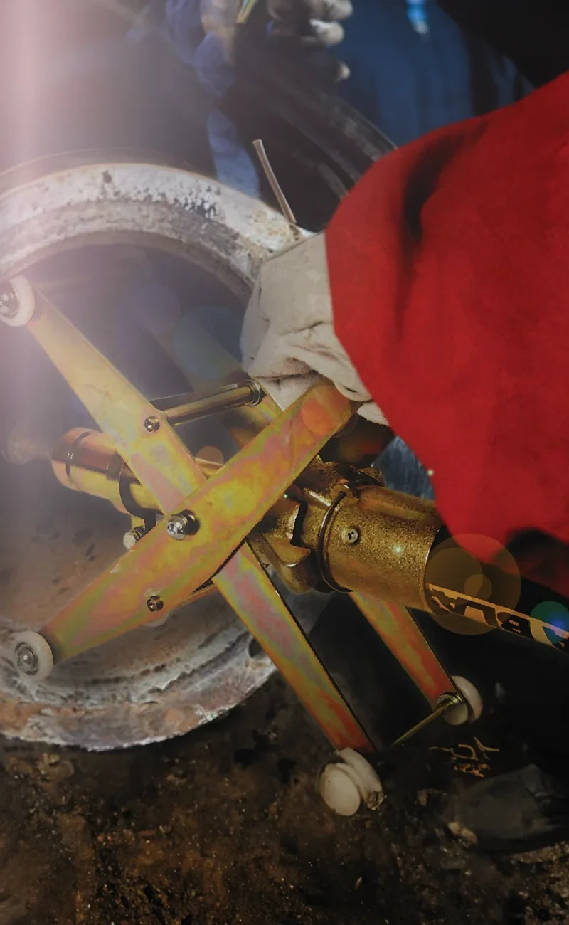 En arbetare i handskar använder ett metallverktyg på ett stort industrirör eller en fläns.