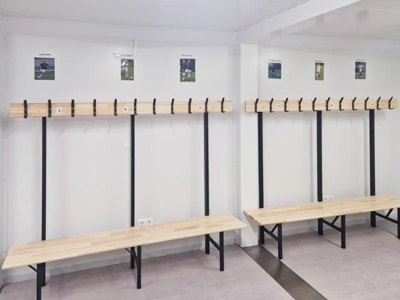 Tomt ombytesrum med träbänkar, väggkrokar och foton av idrottare ovanför varje sektion.