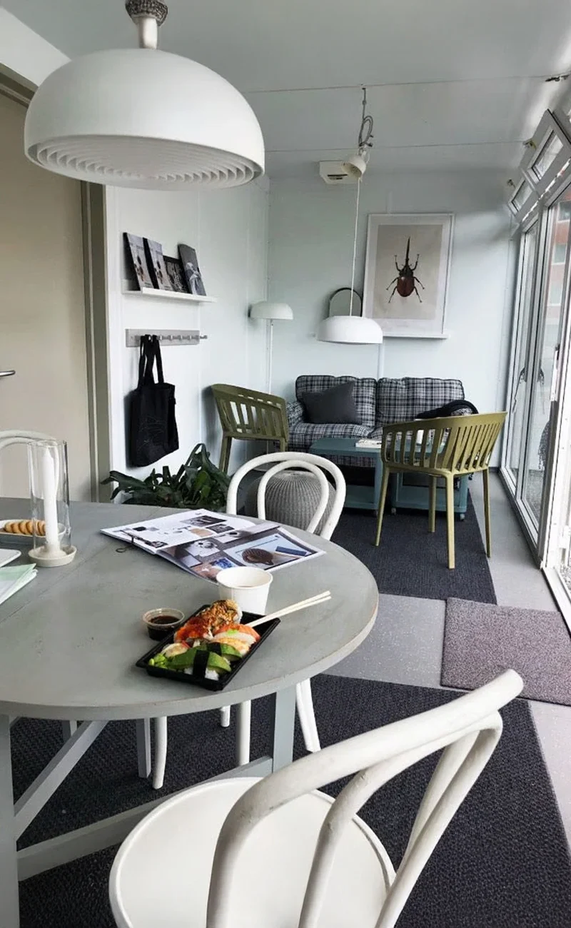 Modern, ljus matplats med sushi på bordet och en mysig sittgrupp med gröna stolar i bakgrunden, perfekt för ett showroom eller med snygga glasmoduler.