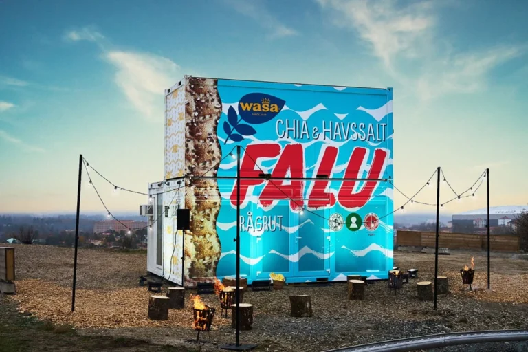 En blå Wasa-behållare med CHIA & HAVSSALT FALU RÅGBRÖT står utomhus i solnedgången med ljusslingor, vilket gör att den sticker ut bland eventmodulerna.