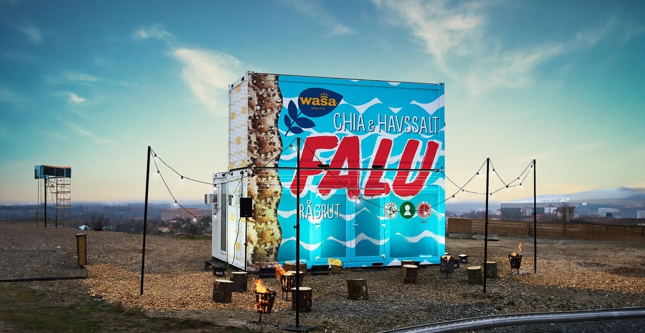 En färgglad fraktcontainer dekorerad med Wasas varumärke står på en grusplan med ljusslingor och sittplatser, vilket skapar en livlig eventatmosfär som påminner om moderna mässmoduler.