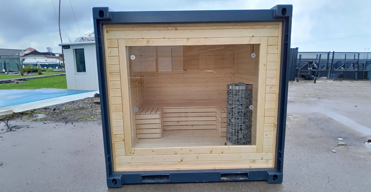 En container som byggts om till en träbastu med bänkar och en metallkamin, sedd framifrån.