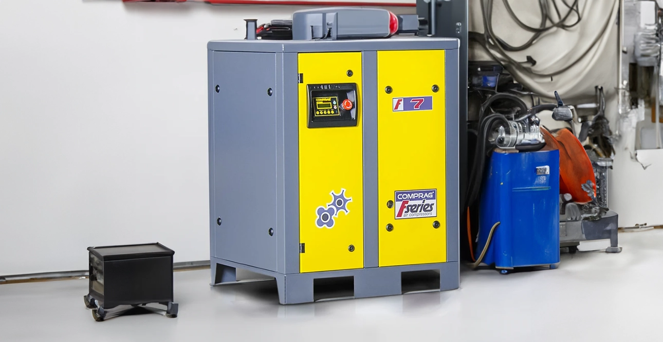 Gul och grå industriell luftkompressormaskin i en verkstadsmiljö, med utrustning i bakgrunden.
